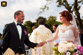 At Baronesse Tacco in Italy, a bride and groom face each other during their wedding ceremony. The photo shows the couple in a moment of exchange.